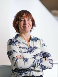 Frau Vergniory mit verschränkten Armen und kurzem Haar, lächelnd.